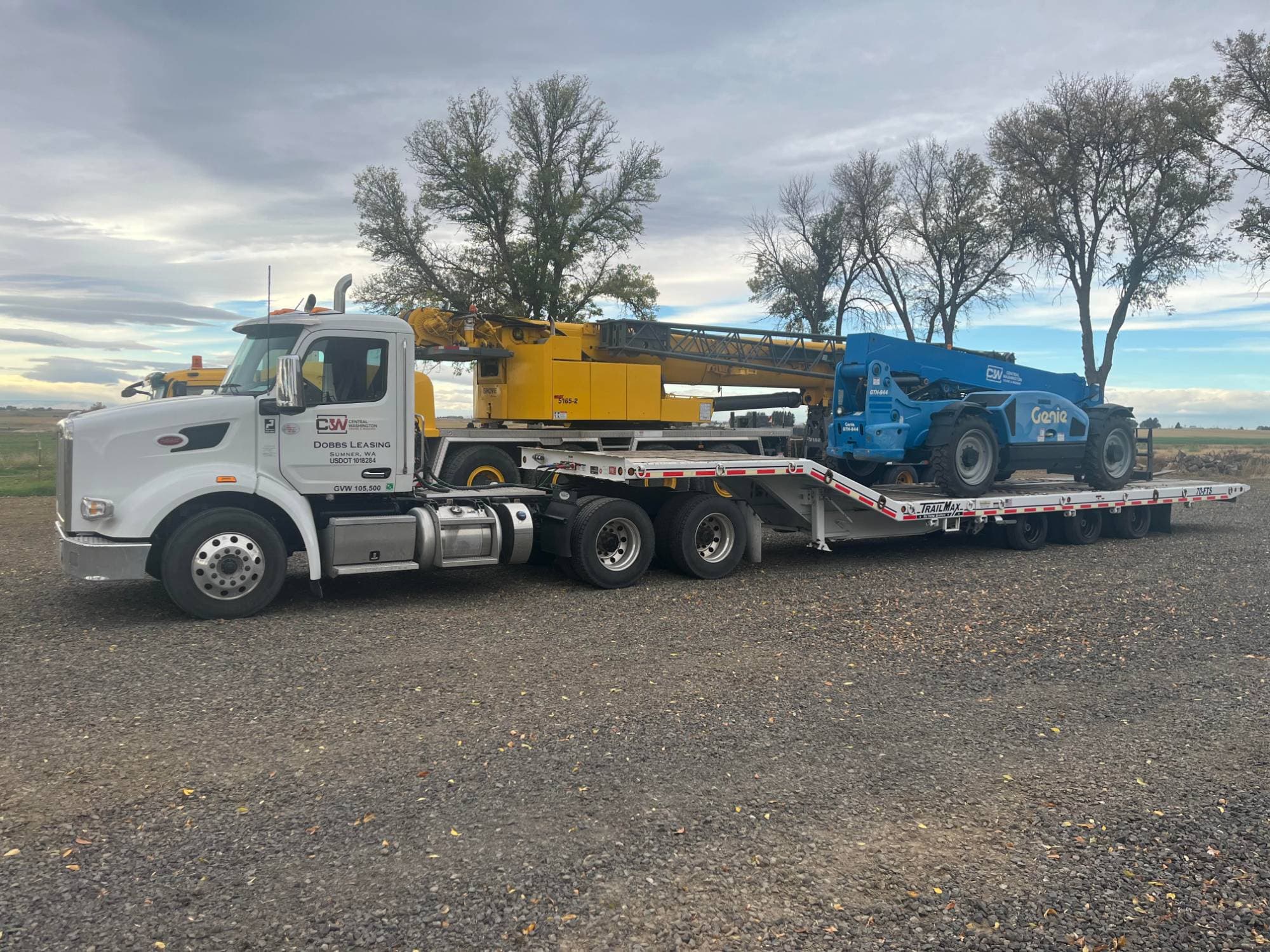CW Crane & Rigging truck and lowboy trailer hauling a Genie GTH-844 telehandler, with the Grove GMK5165-2 all-terrain crane parked behind