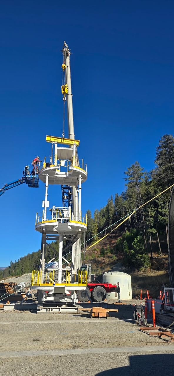Link-Belt 130-ton crane hoisting a multi-deck headframe platform into place while a crew member works from a boom lift