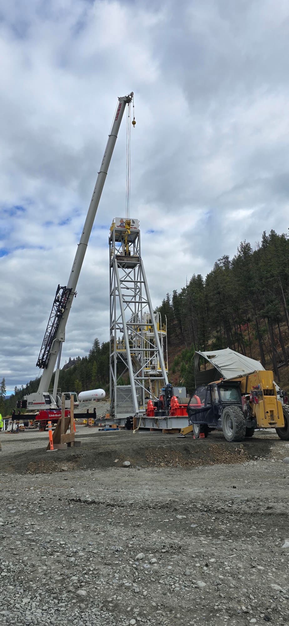 Link-Belt 130-ton rough-terrain crane rigged over a steel mine headframe during assembly at a forested hillside site