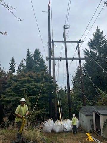 CW Crane & Rigging crew in hard hats and hi-vis handling tag lines on a pole set near energized power lines