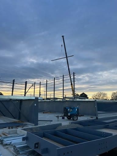 Crane setting structural steel at dusk on a commercial construction project
