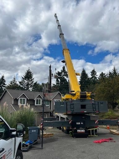 All-terrain crane set up on outriggers beside a CW Crane & Rigging service truck on a tight residential site