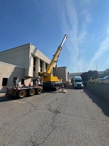 All-terrain crane set up in a tight alley alongside a commercial building for a rooftop lift