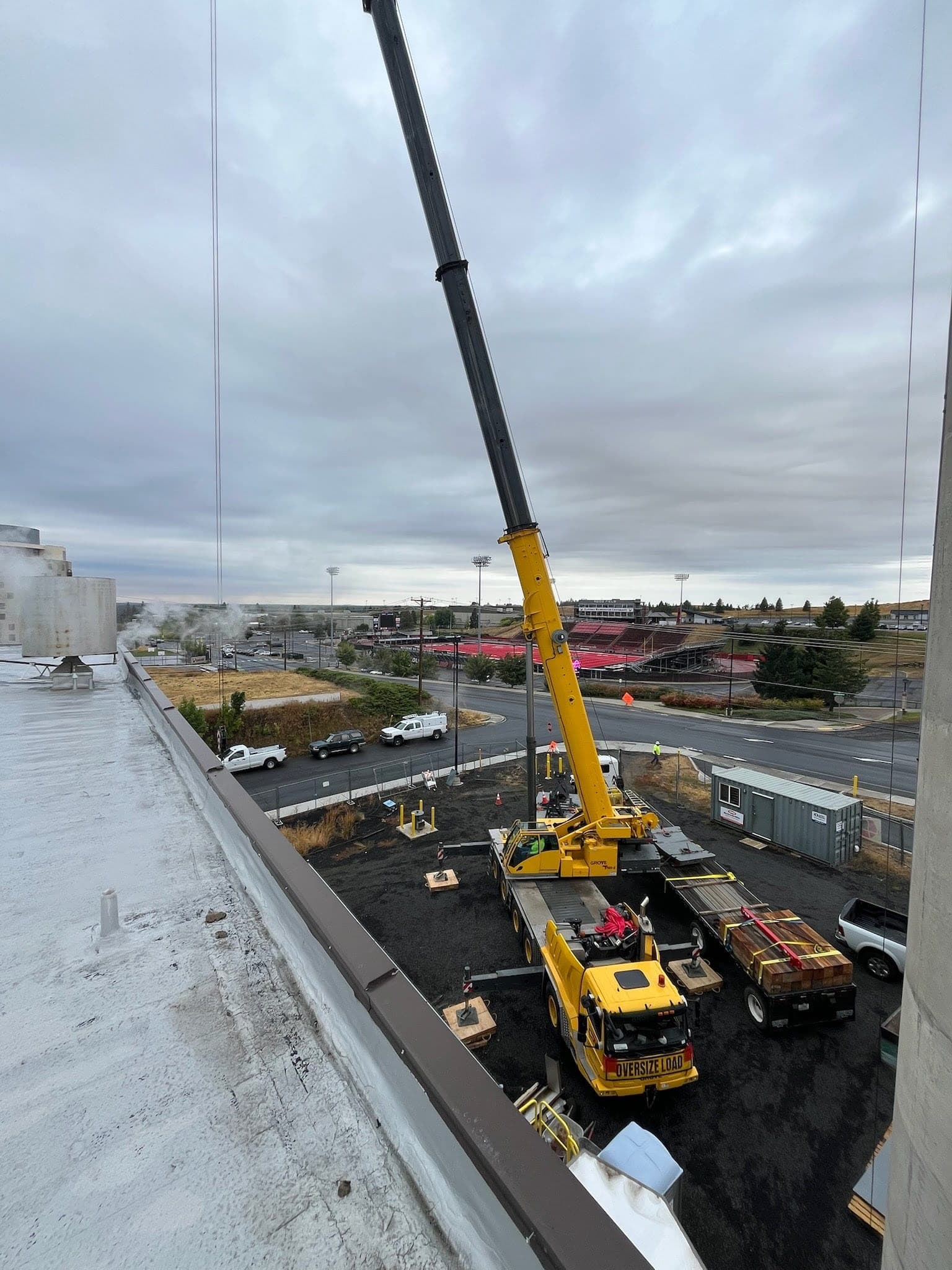 Rooftop view of a Grove all-terrain crane setting mechanical equipment on a commercial building